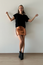 Cargar imagen en el visor de la galería, Modelo mujer usando falda corta metalizada color cobre Fran del Solar, outfit elegante con botines negros, fondo minimalista claro