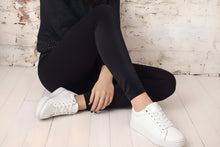 Cargar imagen en el visor de la galería, legging de terciopelo negro tiro alto mujer sentado mostrando ajuste y calce con zapatillas blancas