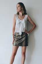 Cargar imagen en el visor de la galería, Modelo usando falda corta de cuerina animal print con blusa blanca, posando en interior sobre fondo claro
