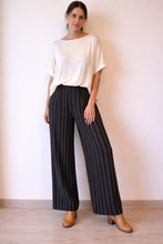 Cargar imagen en el visor de la galería, Mujer usando pantalón de lino negro con rayas verticales, calce suelto y pretina elasticada.
