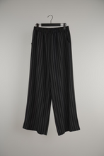 Cargar imagen en el visor de la galería, Mujer usando pantalón de lino negro con rayas verticales, calce suelto y pretina elasticada.