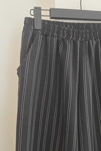 Cargar imagen en el visor de la galería, Mujer usando pantalón de lino negro con rayas verticales, calce suelto y pretina elasticada.
